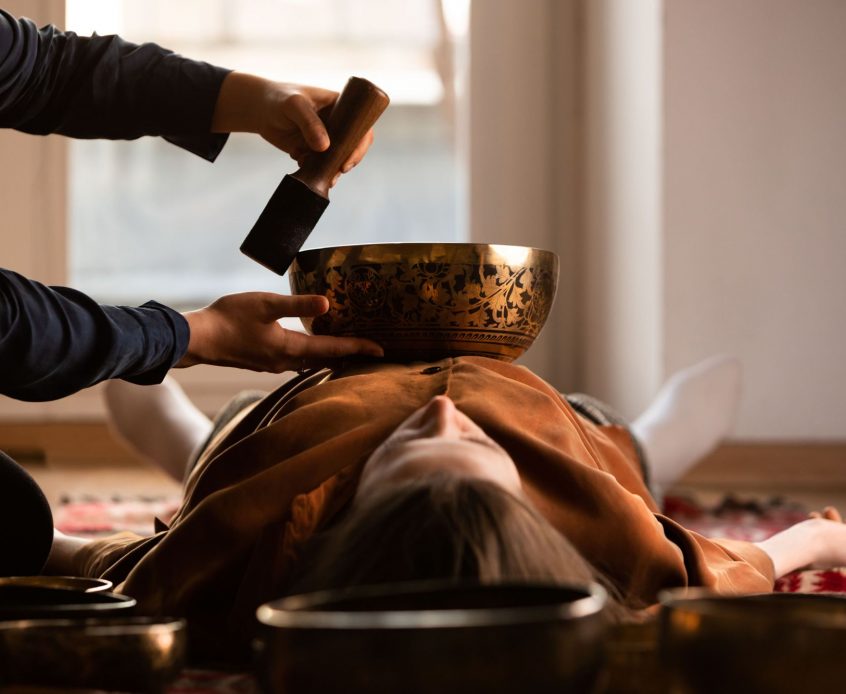 Woman making relaxing massage, meditation, sound therapy with tibetian singing bowls. Stress relief. Selective focus on bowl. Bottom view.